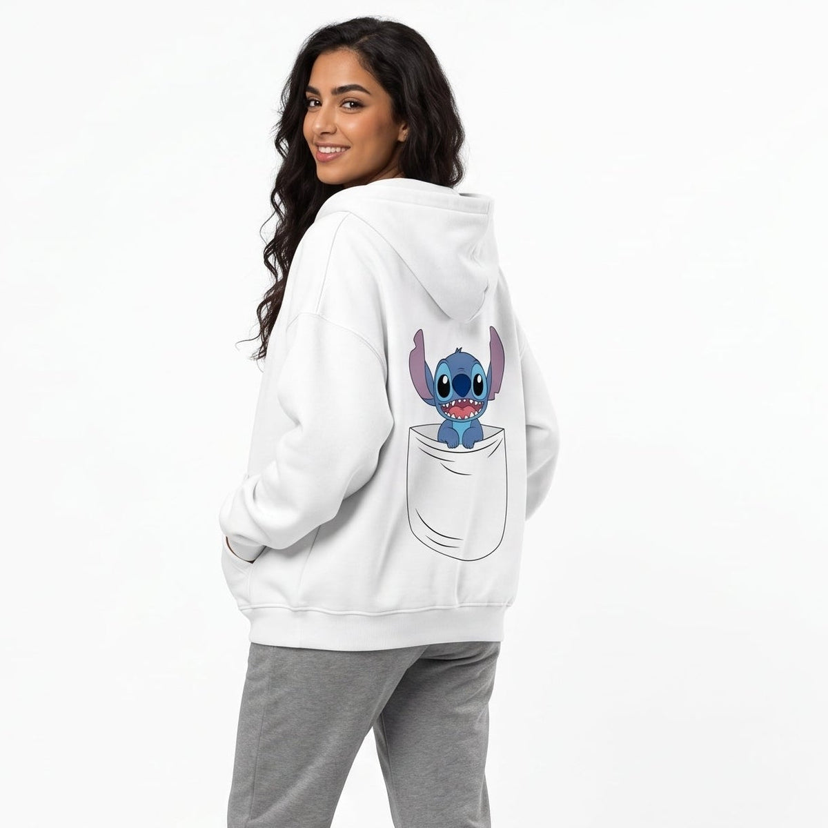 A woman modeling a white hoodie from the back, featuring a graphic of Stitch popping out of a pocket on the back. She is wearing gray sweatpants and white sneakers against a plain white studio background.