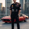 A man stands on a rooftop wearing a black Ferrari Racing team tracksuit with red and white sponsor logos, posed in front of a red Ferrari sports car with a city skyline in the background.